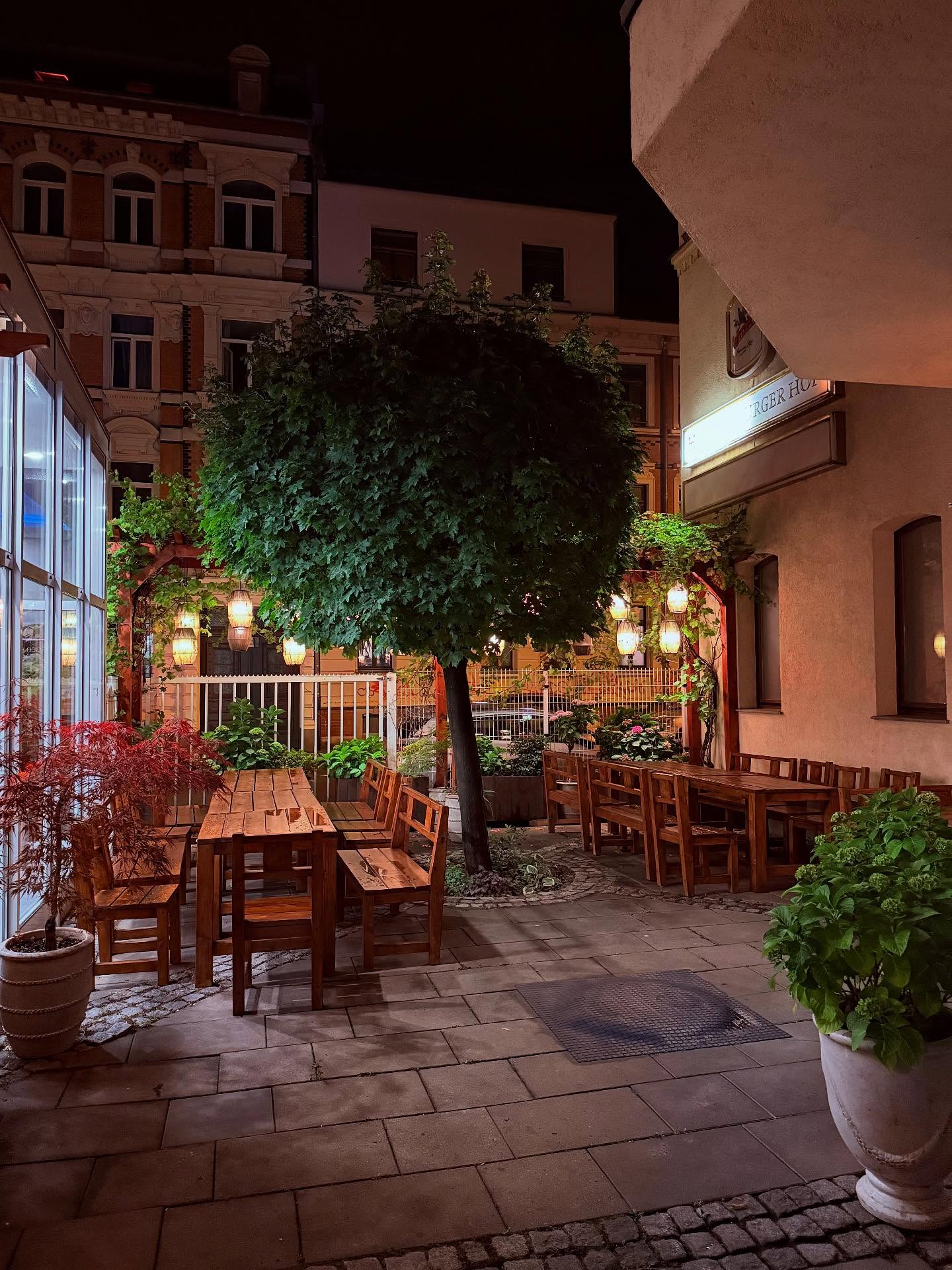 Ruhiger Hinterhof-Garten von Mami Viet in Leipzig-Lindenau mit Holztischen, Baum und Laternen am Abend Ruhiger Hinterhof-Garten von Mami Viet in Leipzig-Lindenau mit Holztischen, Baum und Laternen am Abend